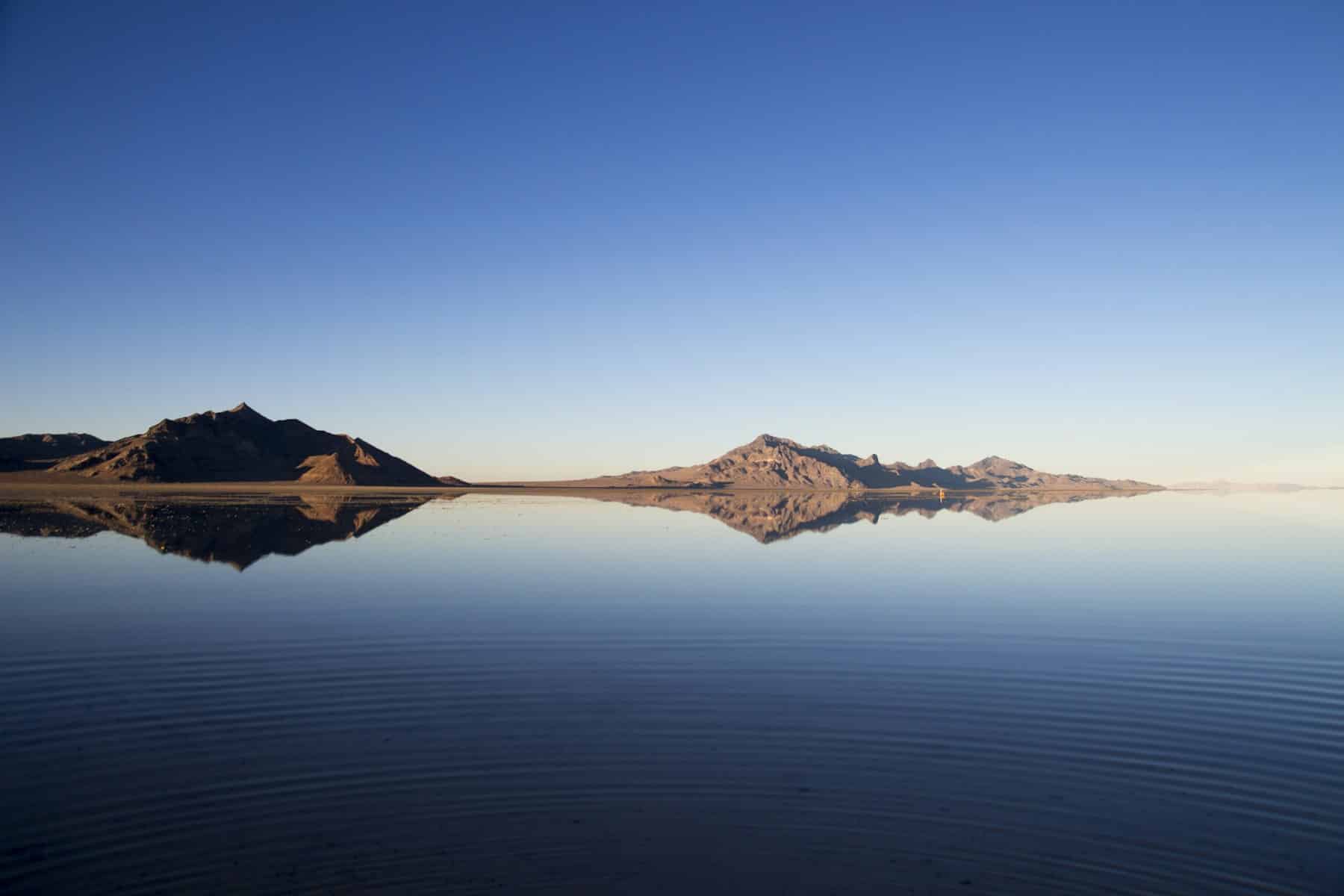Mountains reflected in still blue water beneath a clear sky